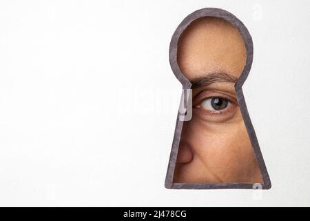 Das Auge der Frau guckt durch das Schlüsselloch, das auf ein Stück Papier gezeichnet ist Stockfoto