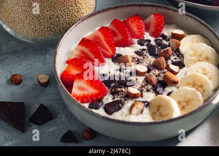 Hirsebrei mit Erdbeere, Banane, dunklen Schokoladenstücken, Haselnuss und Mandel in einer Keramikschale Stockfoto