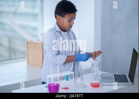 Ein dunkelhaariger Junge in einem Labormantel, der während eines chemischen Experiments beschäftigt aussieht Stockfoto