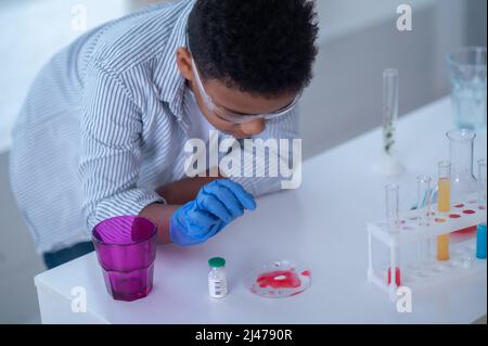 Ein Junge in einem Labormantel, der mit Reagenzgläsern arbeitet und dabei aussieht Stockfoto