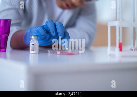 Ein Junge in einem Labormantel, der mit Reagenzgläsern arbeitet und dabei aussieht Stockfoto