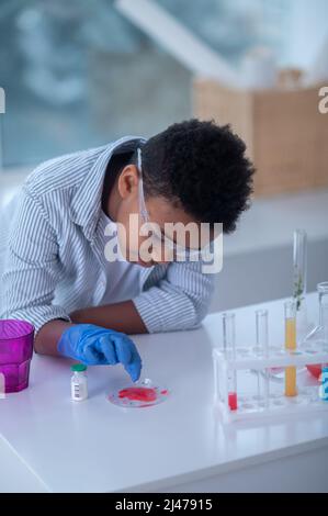 Ein Junge in einem Labormantel, der mit Reagenzgläsern arbeitet und dabei aussieht Stockfoto