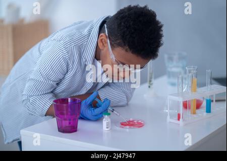 Ein Junge in einem Labormantel, der mit Reagenzgläsern arbeitet und dabei aussieht Stockfoto