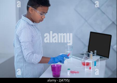 Ein Junge in einem Labormantel, der mit Reagenzgläsern arbeitet und dabei aussieht Stockfoto