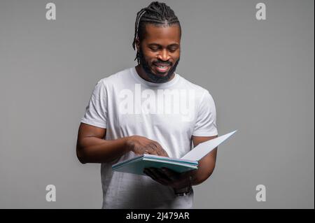 Fokussierter, zufriedener Student, der an der Wand steht und liest Stockfoto