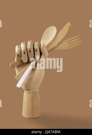Holzhand mit Bambuslöffel, Messer und Gabel auf beigem Hintergrund. Das Konzept der Zero Waste ohne Kunststoff. Umweltfreundliches Besteck. Stockfoto