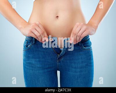 Vielleicht ist es Zeit für eine Diät. Aufnahme einer nicht identifizierbaren jungen Frau, die ihre Jeans im Studio knöpfte. Stockfoto