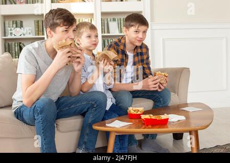 Ein nettes drei Teenager Jungen, essen Fast Food im Wohnzimmer, Fernsehen Stockfoto