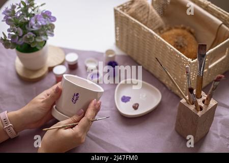 Frauenhänden halten einen weißen Blumenkeramiktopf auf dem Tisch Stockfoto