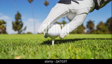 Hand in Golfhandschuhen setzen Golfball auf Tee im Golfplatz. Golfball ist auf Tee auf grünem Rasen Hintergrund. Stockfoto