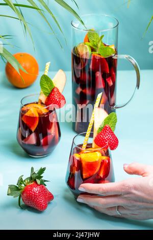 Weibliche Hand hält ein Glas mit traditionellem spanischen Sangria-Cocktail, verziert mit Stücken frischer Erdbeere, einer Prise Minze und Stroh aus Öko-Papier. Stockfoto