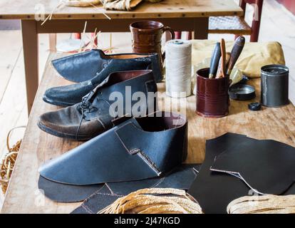 Arbeitstisch mit Vintage-Schuster und Koloniallederschuhen im Sturbridge Village, Massachusetts, USA, in Arbeit Stockfoto