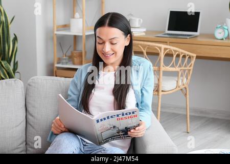 Schöne Frau mit Zahnspangen Lesemagazin auf Sofa zu Hause Stockfoto