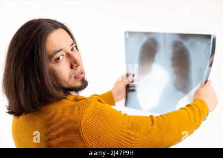 Verwirrt europäischer Mann, der ungläubig auf die Kamera schaut, während er professionelle Lungen-Röntgenaufnahmen hält. Studioaufnahme, weißer Hintergrund. Hochwertige Fotos Stockfoto