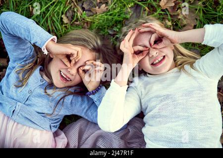 Alles macht Spaß, wenn Sie jung sind. Portrait von zwei kleinen Schwestern, die draußen auf dem Gras liegen. Stockfoto