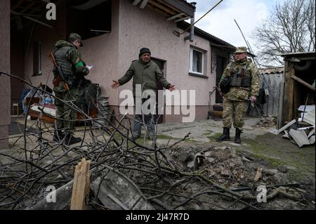 Andriivka, Kiew, Ukraine. 12. April 2022. Ein Mann sah, wie er den Offizieren von Explosionen in seinem Hof berichtete.das Dorf Andriivka, westlich von Kiew, enthüllte schwere Schäden, Tötungen von Zivilisten und das Verschwinden, nachdem die Russen Ende März 2022 ausgetreten waren. Anwohner sowie Militär- und Sicherheitskräfte führen Kontrollen durch, um die Situation einzuschätzen. (Bild: © Valeria Ferraro/ZUMA Press Wire) Stockfoto