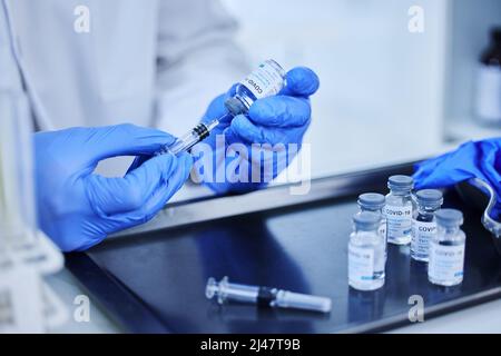 Es ist an der Zeit, sich impfen zu lassen. Zugeschnittenes Bild eines nicht erkennbaren Wissenschaftlers mit einer Spritze, um den covid 19-Impfstoff aus einer Flasche im Labor zu extrahieren. Stockfoto