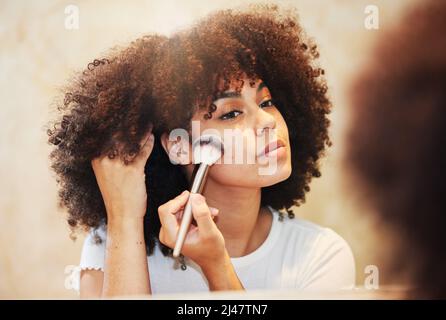 Ich möchte heute so schön leuchten wie die Sonne. Aufnahme einer schönen jungen Frau mit einem Make-up-Pinsel auf ihrem Gesicht. Stockfoto