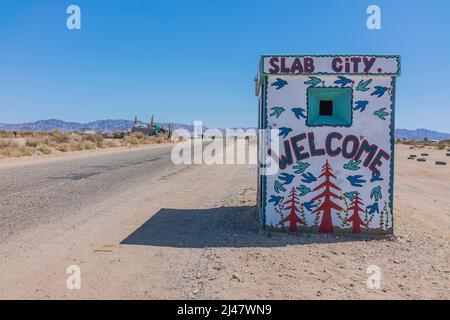 Ein winziges Gebäude mit einem Wandgemälde, das Besucher in Slab City willkommen heißt. Es ist eine netzunabhängige Gemeinde ohne kommunale Dienste. Es bekommt es nam Stockfoto