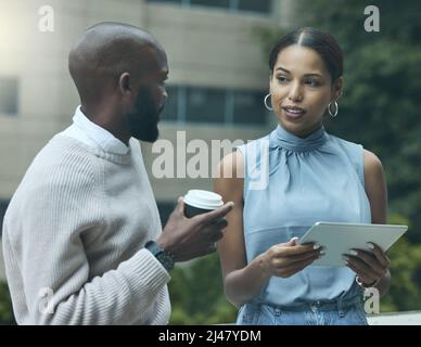 Das Geschäft immer im Blick. Aufnahme von zwei Geschäftsleuten, die vor einem Büro ein digitales Tablet benutzen. Stockfoto