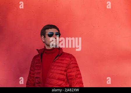Junger Mann in rotem Pullover und Jacke in der Nähe der roten Wand Stockfoto