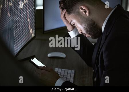 In der verzweifelten Notwendigkeit einiger guter Nachrichten. Aufnahme eines jungen Händlers, der sein Smartphone benutzte, während er den Aktienmarkt überwachte. Stockfoto