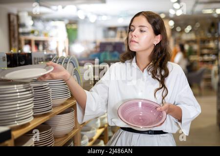 Frau wählt Teller im Geschirrladen Stockfoto
