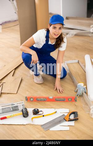 Eine Bauarbeiterin stellte Holzlaminatplatte auf den Boden Stockfoto