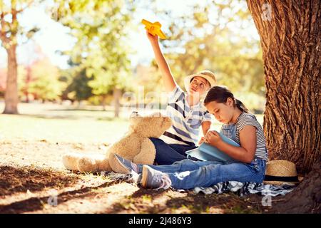 Genießen Sie ihre eigenen kleinen Abenteuer im Park. Aufnahme von zwei kleinen Geschwistern, die Spaß haben, während sie auf einer Decke im Park sitzen. Stockfoto