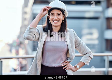 Wenn Sie den Hardhut tragen, dann tun Sie harte Arbeit. Aufnahme einer jungen Geschäftsfrau, die einen Hardhut trägt, während sie draußen steht. Stockfoto