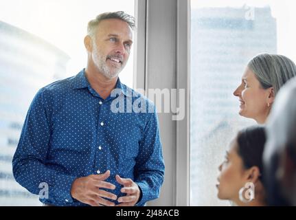 Also, wie geht's weiter? Eine kurze Aufnahme eines gutaussehenden, reifen Geschäftsmannes, der sich im Büro an seine Kollegen wendet. Stockfoto