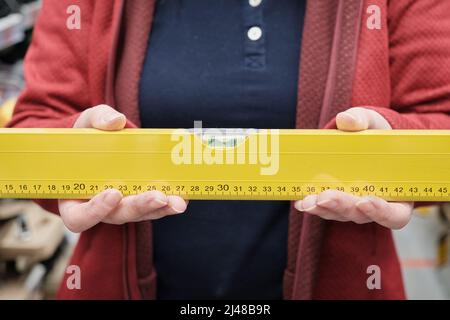 Frau im Geschäft wählt Ebene zu kaufen, um einen glatten Horizont zu bestimmen. Nahaufnahme der Hände Stockfoto