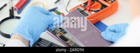 Meister öffnet die hintere Abdeckung des Mobiltelefons in der Nähe der Werkstatt Stockfoto