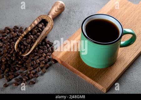 Grüne Tasse Kaffee mit Kaffeebohnen auf betonem Hintergrund Stockfoto