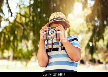 Die Welt in einem neuen Licht zu sehen. Aufnahme eines kleinen Jungen, der mit einer Vintage-Kamera im Park ein Foto gemacht hat. Stockfoto