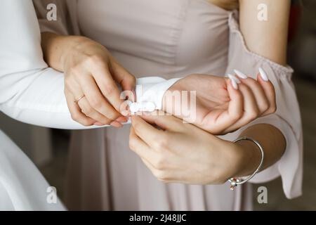 Freundin hilft der Braut, ein Hochzeitskleid zu tragen, indem sie die Ärmel knöpft. Stockfoto