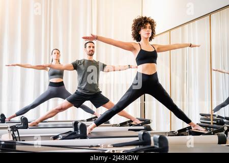Pilates-Klasse von verschiedenen Menschen tun stehende Yoga-Posen auf Reformer Betten in einem Fitnessstudio in einem Gesundheits-und Fitness-Konzept Stockfoto
