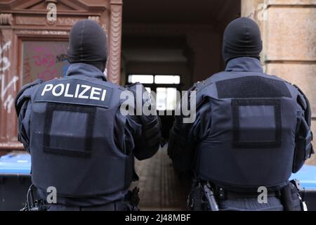 Dresden, Deutschland. 13. April 2022. Zwei Polizisten stehen vor einem Hauseingang.im Zusammenhang mit Unruhen im vergangenen Mai durchsucht die sächsische Polizei seit dem frühen Mittwochmorgen Wohnungen in Dresden, Görlitz, Zwickau und Chemnitz. Eine große Anzahl von Verdächtigen wird wegen des Verdachts einer Verletzung des Friedens in einem besonders schweren Fall untersucht. Die Polizei sagte, dass 300 Beamte an den Durchsuchungen beteiligt waren. Quelle: Tino Plunert/dpa/Alamy Live News Stockfoto