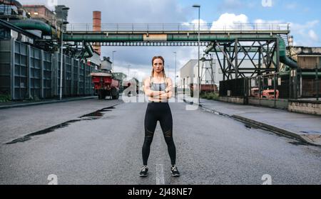 Eine Sportlerin aussehende Kamera, die vor einer Fabrik posiert Stockfoto