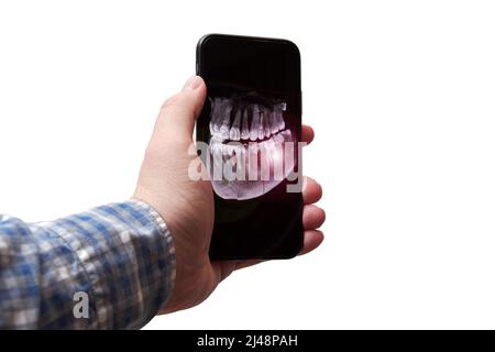 Die Hand des Mannes, der ein Mobiltelefon mit einem Röntgenbild seines Kiefers und Zahns hält. Hervorhebung von Schmerzflecken. Zahnarzt und medizinische Analyse Stockfoto