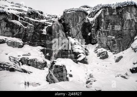Langzeitbelichtung von Wasser in den Bergen im Winter. Schwarzweiß-Fotografie. Wasserfall Skok in der Hohen Tatra, Slowakei. Stockfoto
