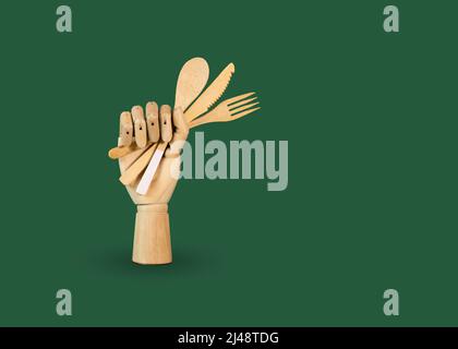 Holzhand mit Bambuslöffel, Messer und Gabel auf grünem Hintergrund. Das Konzept der Zero Waste ohne Kunststoff. Umweltfreundliches Besteck. Banner mit CO Stockfoto