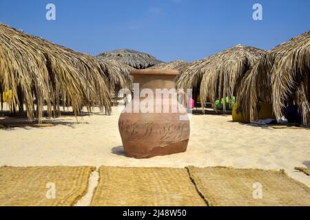 Lehmurne am Strand, vor dem Hintergrund von Sonnenschirmen, die an sonnigen Tagen mit trockenen Palmenblättern bedeckt sind. Nahaufnahme. Selektiver Fokus. Stockfoto