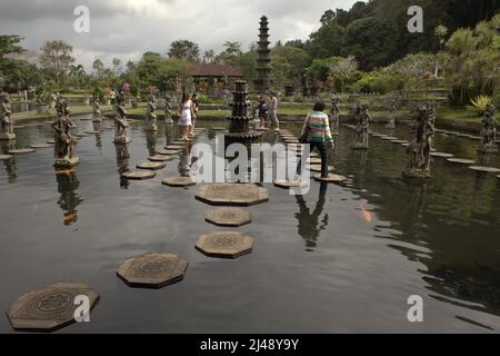 Besucher, die auf steinernen Fußstapfen am Tirta Gangga Wasserpalast in Karangasem, Bali, wandeln. Das Tirta Gangga (tirta bedeutet „heiliges Wasser“; Gangga bezieht sich auf den Ganges in Indien) wurde auf der Grundlage der Überzeugung erbaut, dass Wasser heilig ist, und war ein ehemaliger königlicher Palast des Königreichs Karangasem. Stockfoto