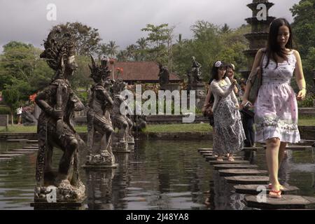 Frauen, die auf Steinspuren im Tirta Gangga Wasserpalast in Karangasem, Bali, spazieren. Das Tirta Gangga (tirta bedeutet „heiliges Wasser“; Gangga bezieht sich auf den Ganges in Indien) wurde auf der Grundlage der Überzeugung erbaut, dass Wasser heilig ist, und war ein ehemaliger königlicher Palast des Königreichs Karangasem. Stockfoto