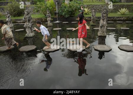 Kinder, die auf Steinspuren im Tirta Gangga Wasserpalast in Karangasem, Bali, spazieren. Das Tirta Gangga (tirta bedeutet „heiliges Wasser“; Gangga bezieht sich auf den Ganges in Indien) wurde auf der Grundlage der Überzeugung erbaut, dass Wasser heilig ist, und war ein ehemaliger königlicher Palast des Königreichs Karangasem. Stockfoto
