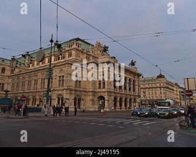 Blick auf das historische Gebäude der berühmten Wiener Staatsoper in Österreich am bewölkten Tag am Abend mit Autos und Menschen vor der Tür. Stockfoto