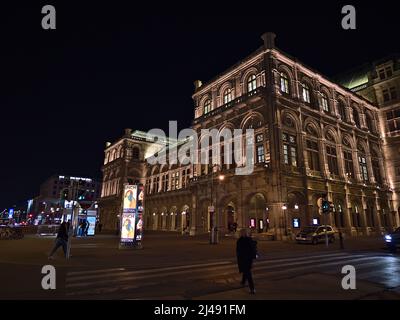 Nachtansicht der berühmten Wiener Staatsoper in Österreich mit beleuchteter Fassade und vorbeiziehenden Menschen in der historischen Innenstadt. Stockfoto