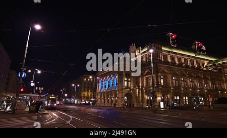 Schöner Blick auf die beleuchtete Fassade der Wiener Staatsoper in Österreich bei Nacht mit Straßenbahn vor dem Haus. Stockfoto