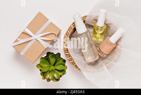 Bio-Kosmetik mit Pflanzen und Geschenken für den Urlaub. Flach liegend, Draufsicht klare Glas-Pumpflasche, Pinsel-Glas, feuchtigkeitsspendende Serum-Glas in einem Papier-Baske Stockfoto